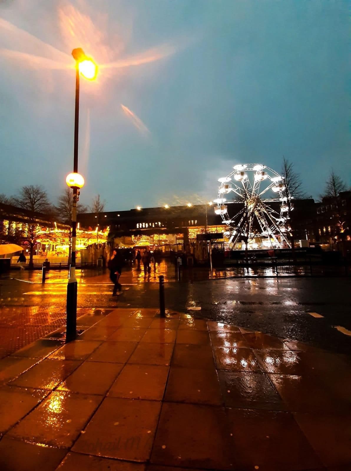 A UK city street at dusk, lit up for the Christmas markets